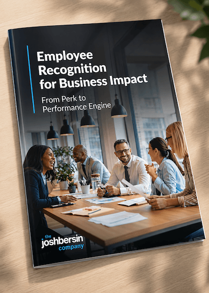 A booklet titled "Employee Recognition for Business Impact" with the subtitle "From Perk to Performance Engine" is displayed on a wooden table. The cover features a diverse group of four individuals engaged in discussion, with office plants and various documents scattered across the table. The setting includes large windows and hanging lamps, suggesting a modern office environment.