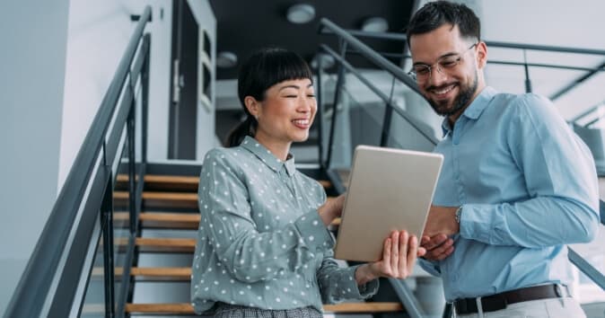 Two people in an office on a stairway looking at a tablet.